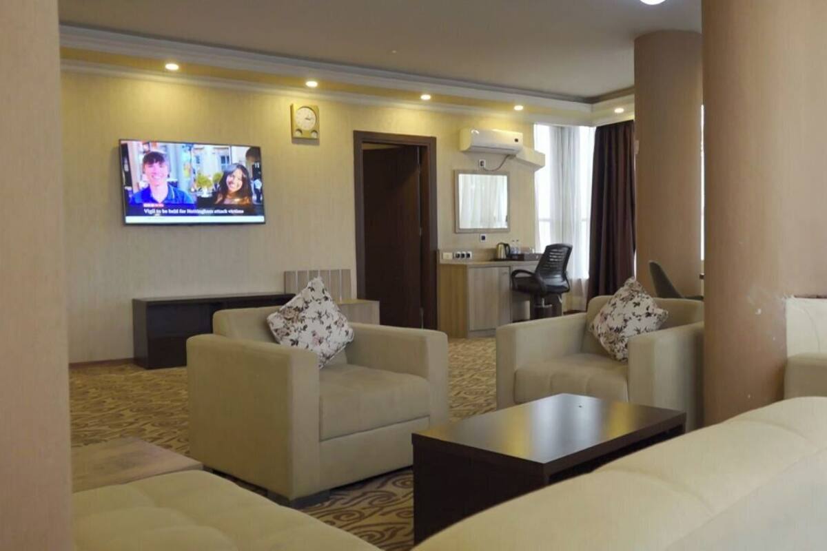 A hotel room with a living area featuring two sofas, a coffee table, a TV mounted on the wall, and a small kitchenette.