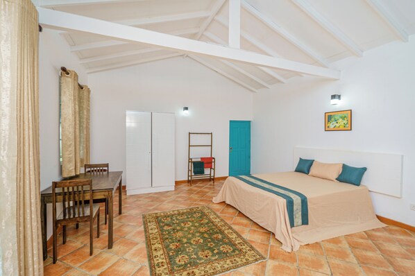 A bedroom with a bed, a desk, chairs, a wardrobe, and a door.