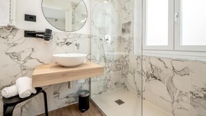 Un baño moderno con salpicadero de mármol, tocador de madera, espejo redondo y ducha con mampara de cristal.