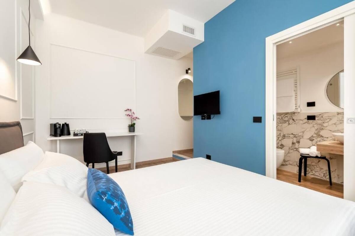 Ein modernes Hotelzimmer mit einem großen Bett, einem Schreibtisch, einem Sessel, einem Fernseher und einem Badezimmer mit Marmorwand.