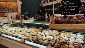 Een vitrine van een bakkerij met diverse gebakjes en een bord waarop de prijzen staan.