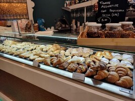 Leipomon esillepanoteline, jossa on erilaisia leivonnaisia, ja kyltti, jossa on hinnat.