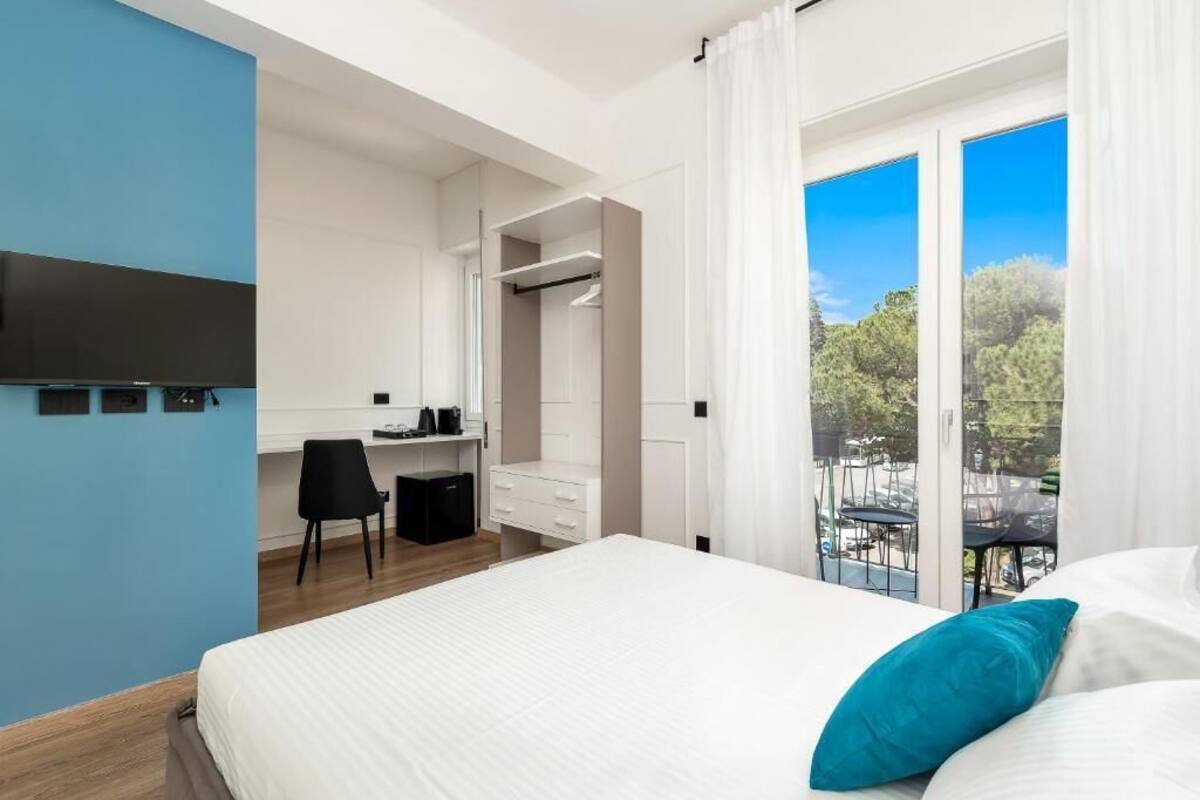 Ein modernes Hotelzimmer mit einem großen Bett, einem Schreibtisch und einem Balkon mit Blick auf Bäume.
