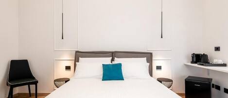 A modern hotel room with a large bed, a chair, a small table, and a coffee machine.