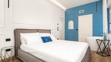 A neatly arranged bedroom with a bed, a bedside table, a mirror, and a bathroom with a sink and toilet.