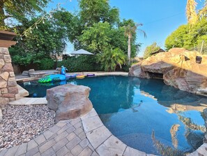 A swimming pool with a pebble-lined deck, surrounded by rocks and trees. - Second Story Suite w/ Balcony (Queen Creek)