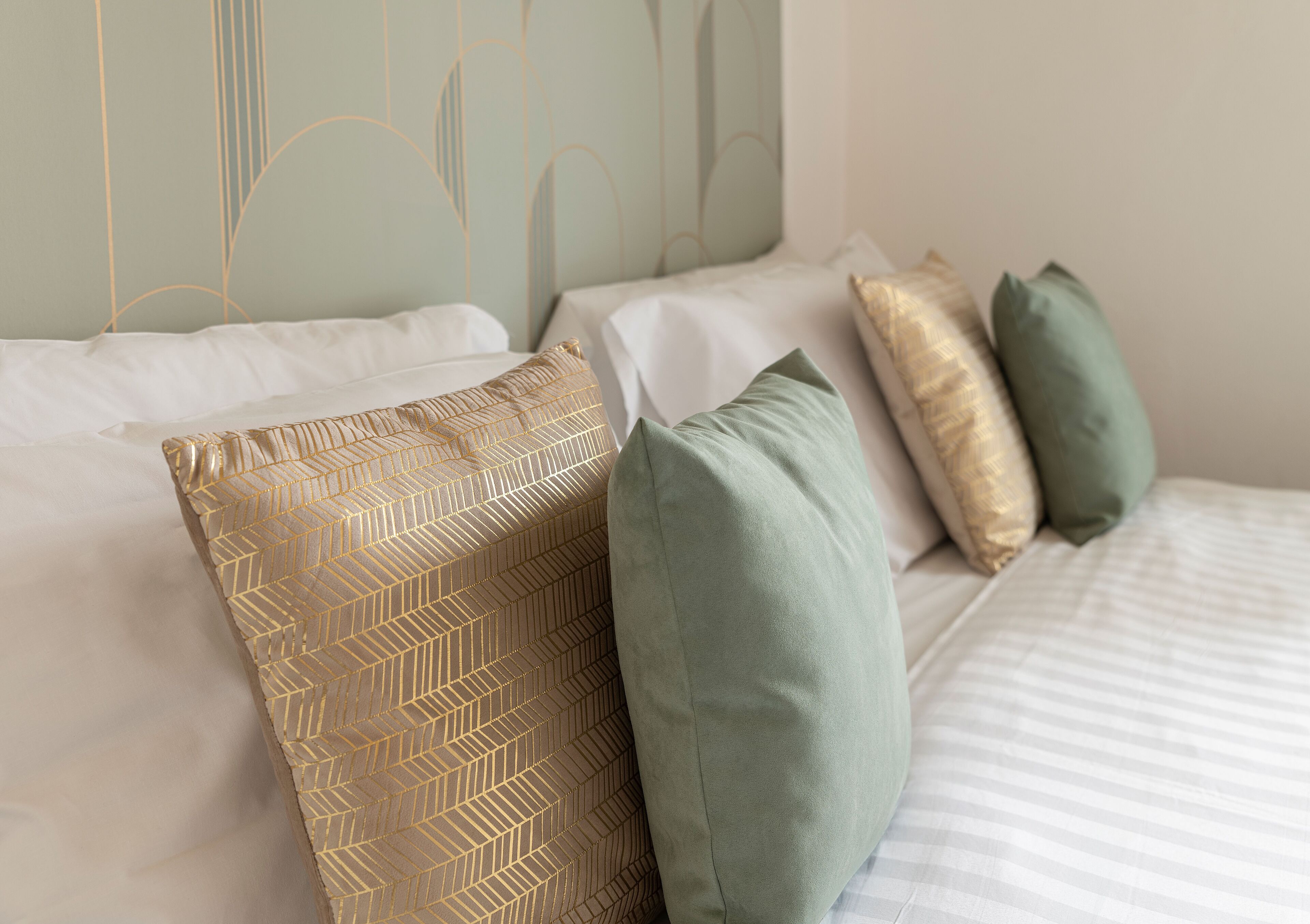 A neatly made bed with white linens and two pillows, one with a gold pattern and one green.
