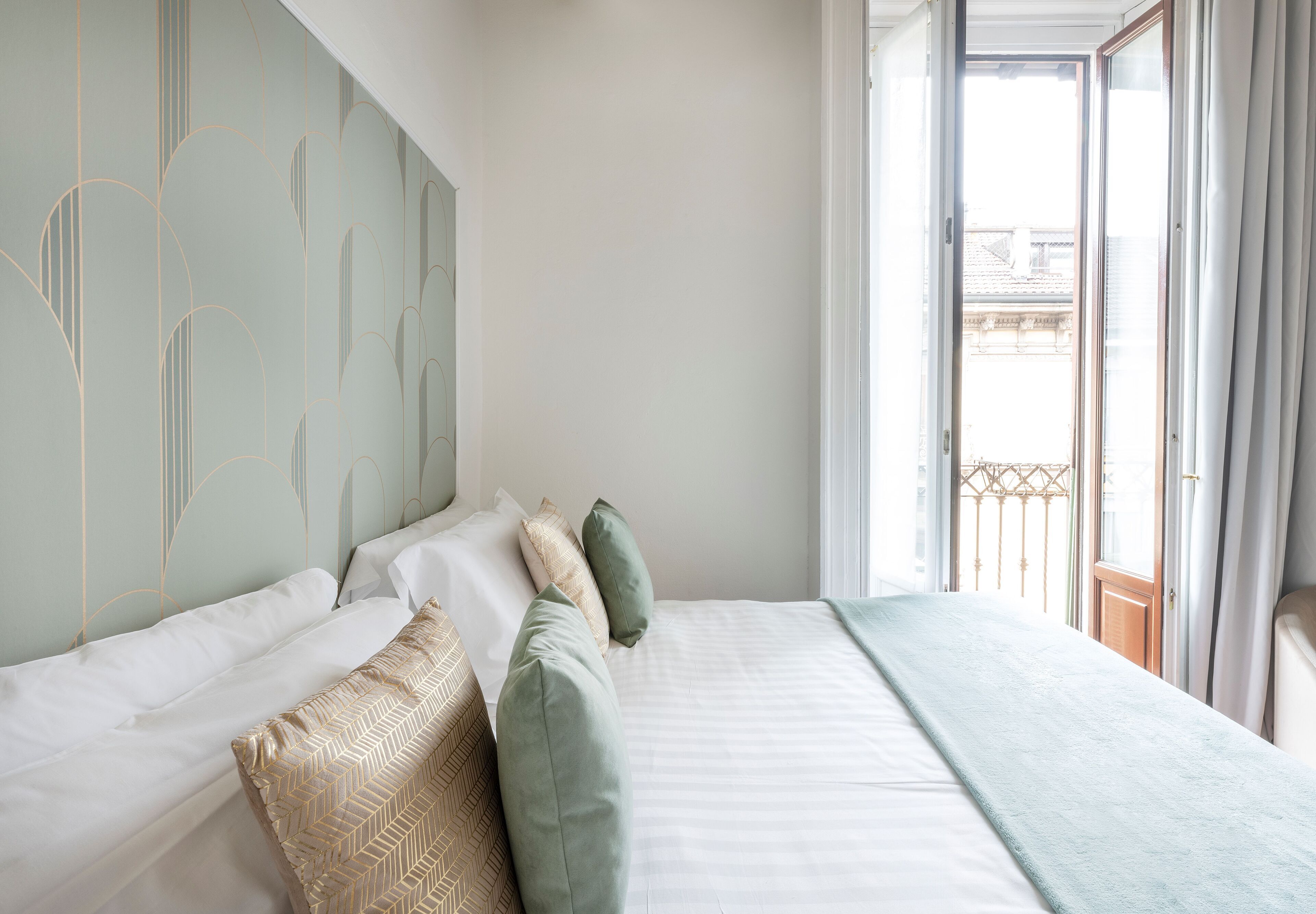 Un lit bien fait, avec une literie blanche et verte, un coussin à motifs et un plaid bleu clair.