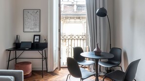 Una sala de estar moderna con un escritorio negro, una computadora portátil, un mapa de Milán, una mesa redonda con sillas y un gran ventanal con cortinas.