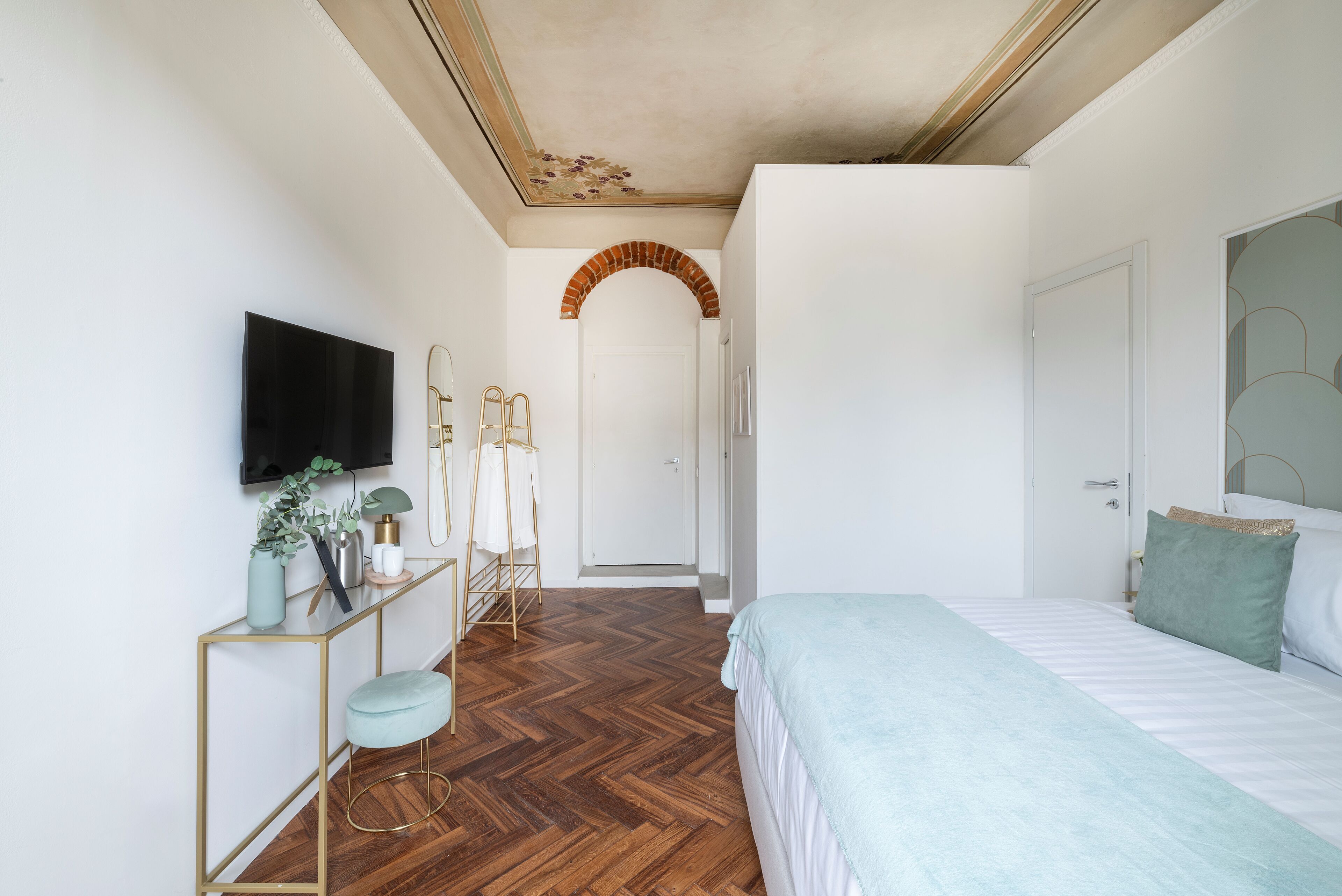 A bedroom with a bed, a TV, a console table with a mirror, and a door leading to another room.