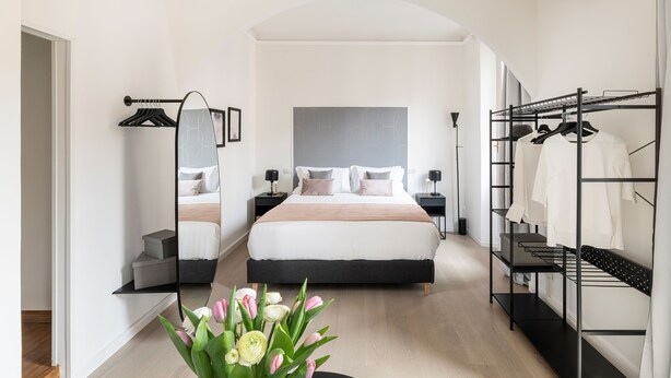 Un dormitorio moderno con una cama grande, un espejo, un armario y un florero con flores.