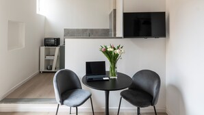 Una cocina moderna con un televisor sobre la encimera, dos sillas alrededor de una mesita y un florero con flores sobre la mesa.