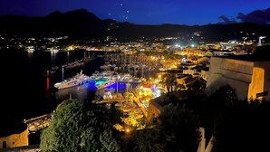 Eine Küstenstadt bei Nacht mit Hafen, Gebäuden und Bergen im Hintergrund.