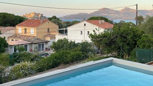Un quartier résidentiel doté d’une piscine, de maisons aux toits recouverts de tuiles rouges et bordé par un paysage montagneux.