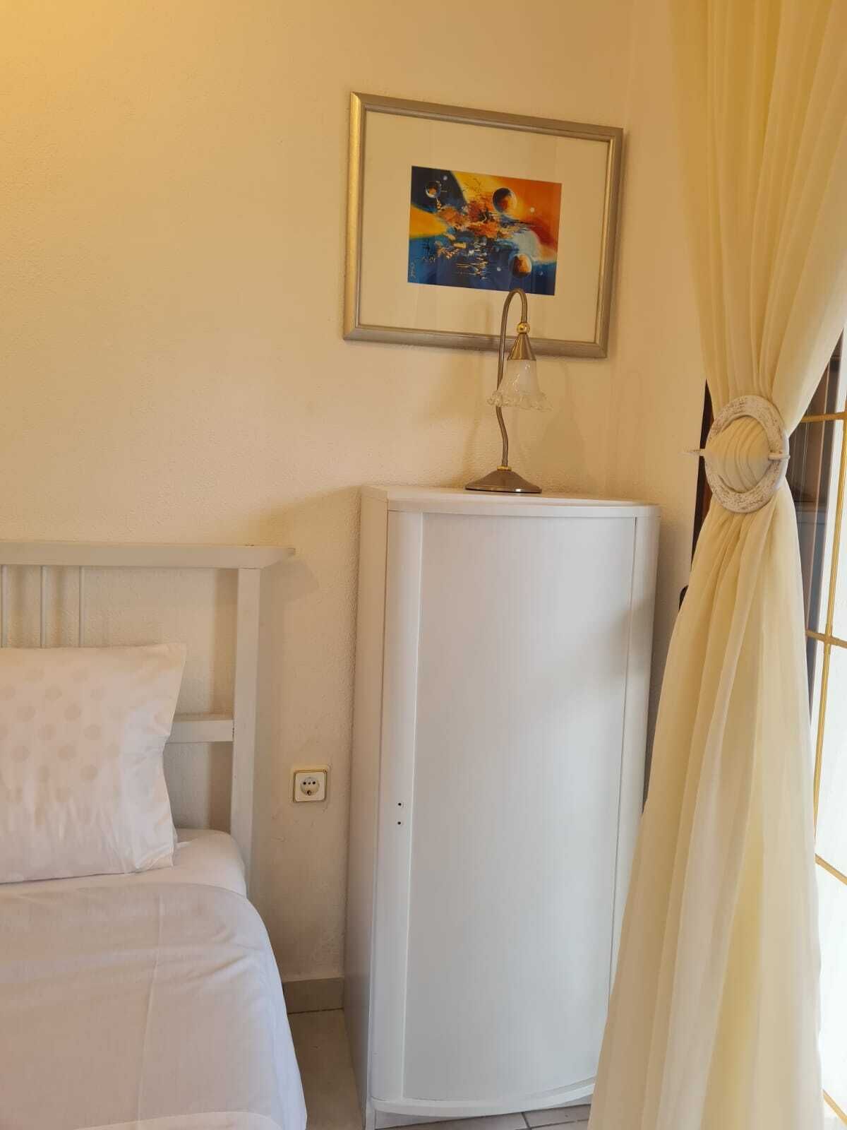 A bedroom with a bed, a white cabinet, and a framed painting on the wall.