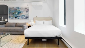 Ein modernes Hotelzimmer mit einem Bett, einer Couch, einem Glastisch und einem großen, abstrakten Gemälde an der Wand.
