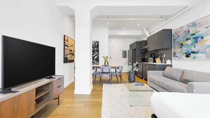 Ein modernes Wohnzimmer mit Flachbildfernseher, einem grauen Sofa und einer Essecke mit Tisch und Stühlen.