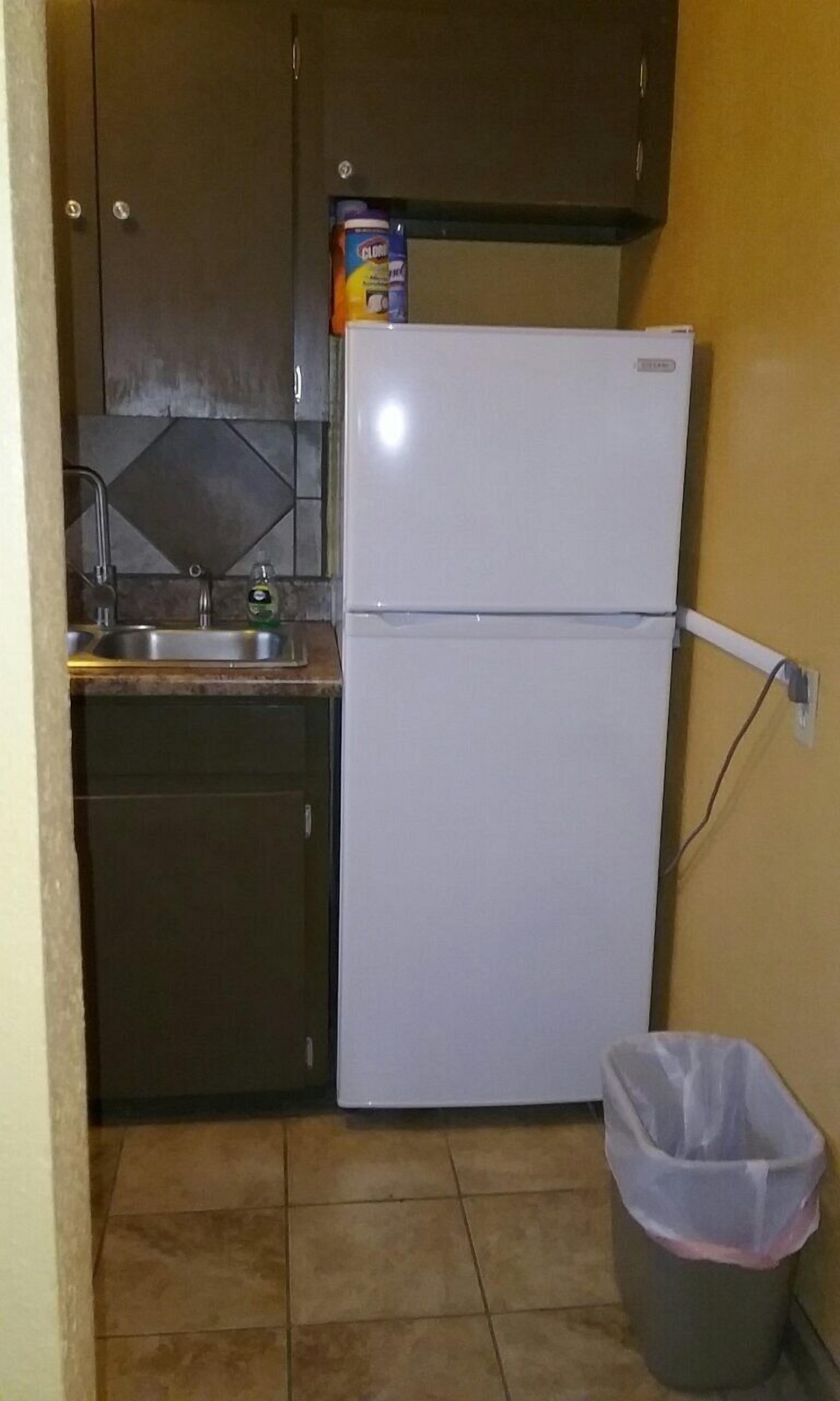 Een kleine keuken met een witte koelkast, een spoelbak en een prullenbak.