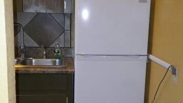 Een kleine keuken met een witte koelkast, een spoelbak en een prullenbak.