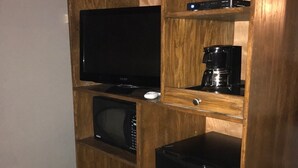 A wooden entertainment center with a flat-screen TV, a coffee maker, a microwave, and a black trash bin.