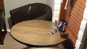 A small, round wooden table with a metal tray and a cup, accompanied by two black leather chairs.