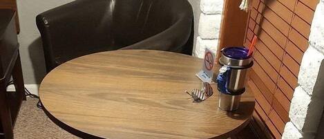 Una pequeña mesa redonda de madera con una bandeja de metal y una taza, junto a dos sillas de cuero negro.