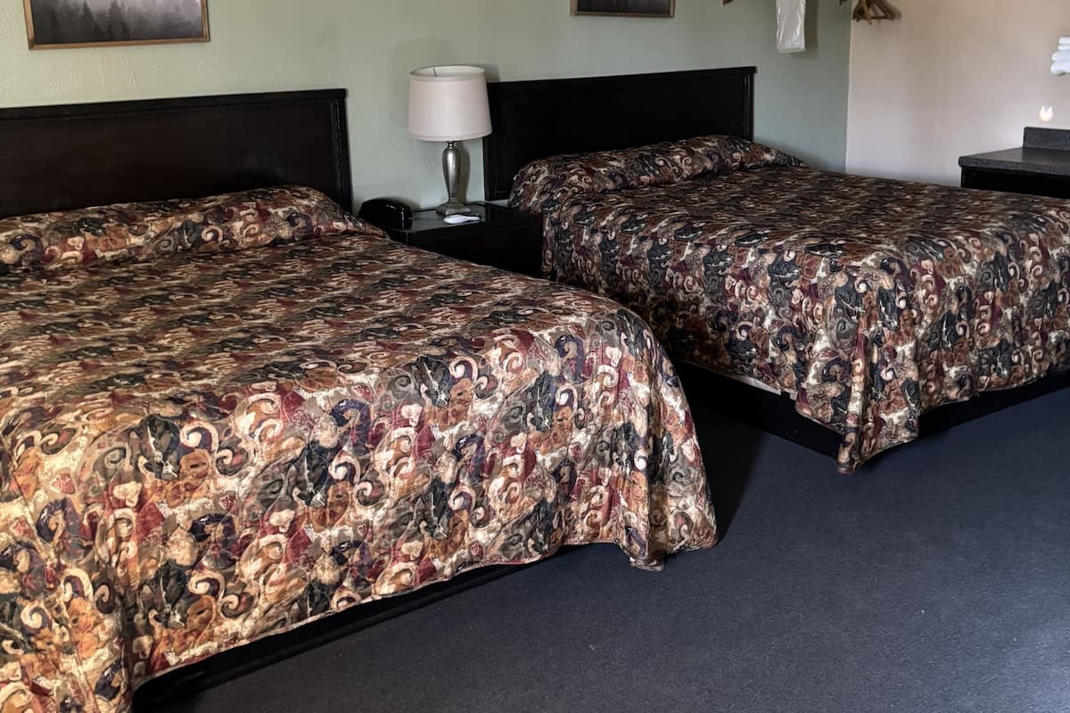 Une chambre d’hôtel avec deux lits, un ventilateur de plafond, une table de chevet avec une lampe et deux tableaux encadrés au mur.