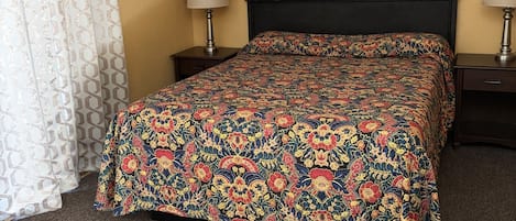 Habitación de hotel con cama, dos mesitas de noche, ventana con cortinas y un cuadro en la pared.