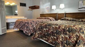 A hotel room with two beds, a bathroom, a wooden headboard, a hanging light fixture, and a wall-mounted mirror.