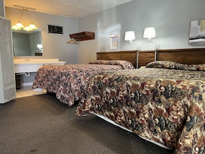 Habitación de hotel con dos camas, un baño, cabecero de madera, lámpara colgante y espejo adosado a la pared.