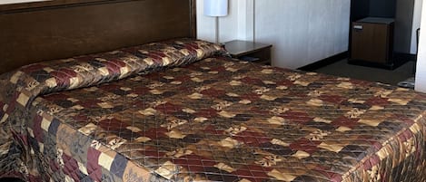 A hotel room with a large bed, a nightstand, a lamp, a painting of a lake, and a coffee machine.