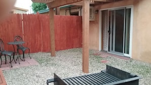 A patio area with a wooden pergola, a red fence, and a sliding glass door leading to a covered space.