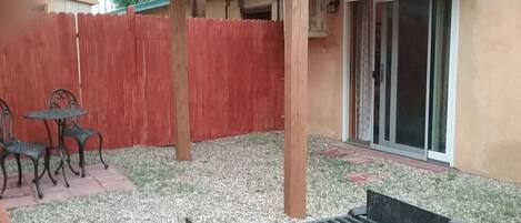 Un patio con una pérgola de madera, una cerca roja y un ventanal corredizo que da a un espacio cubierto.
