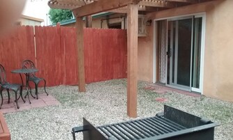 Uma área de pátio com pérgola de madeira, cerca vermelha e porta de correr de vidro que dá para um espaço coberto.