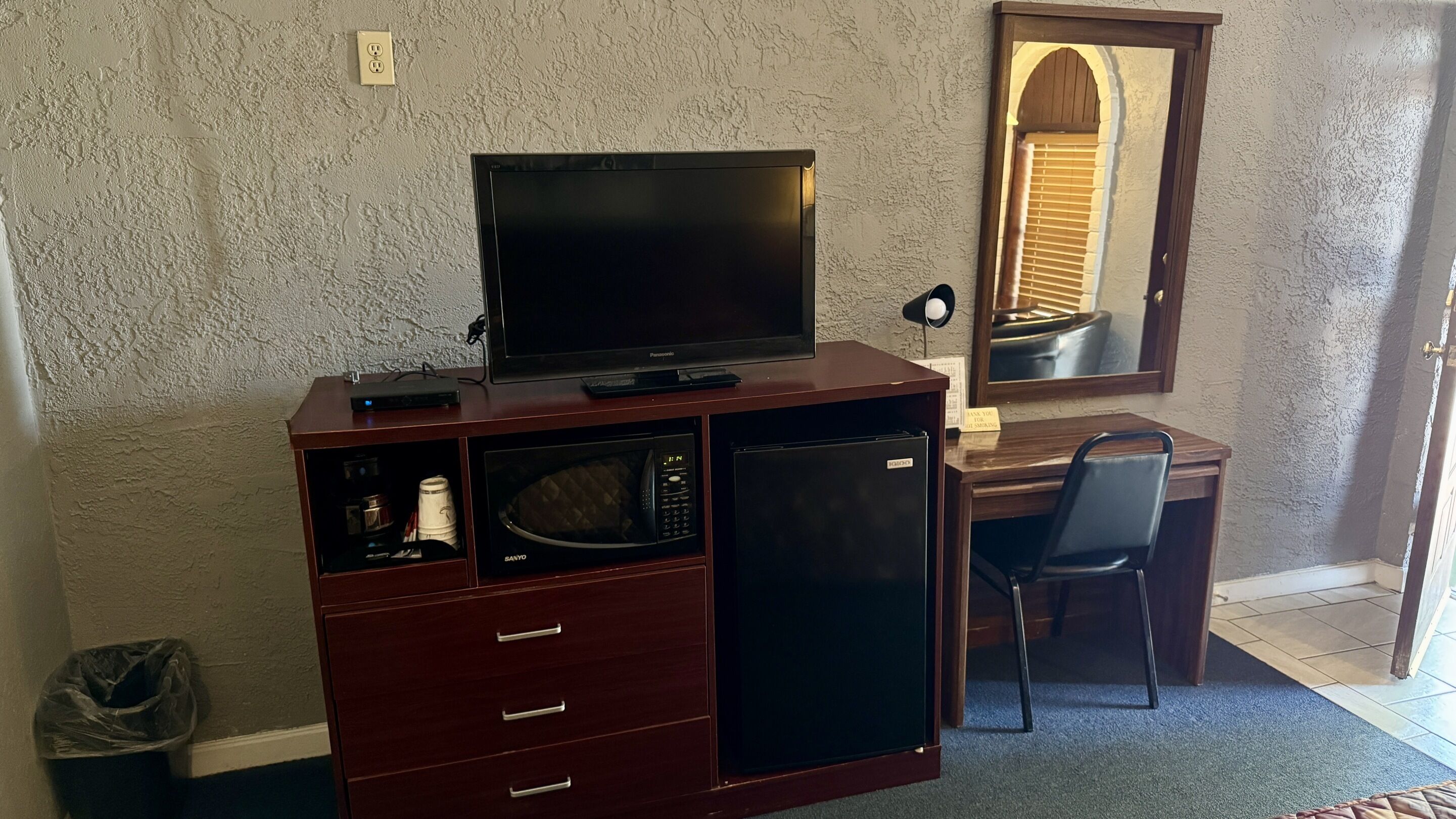 A compact room with a wooden desk, a television, a microwave, and a refrigerator.