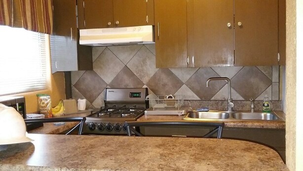 A kitchen with a gas stove, stainless steel sink, and granite countertops.