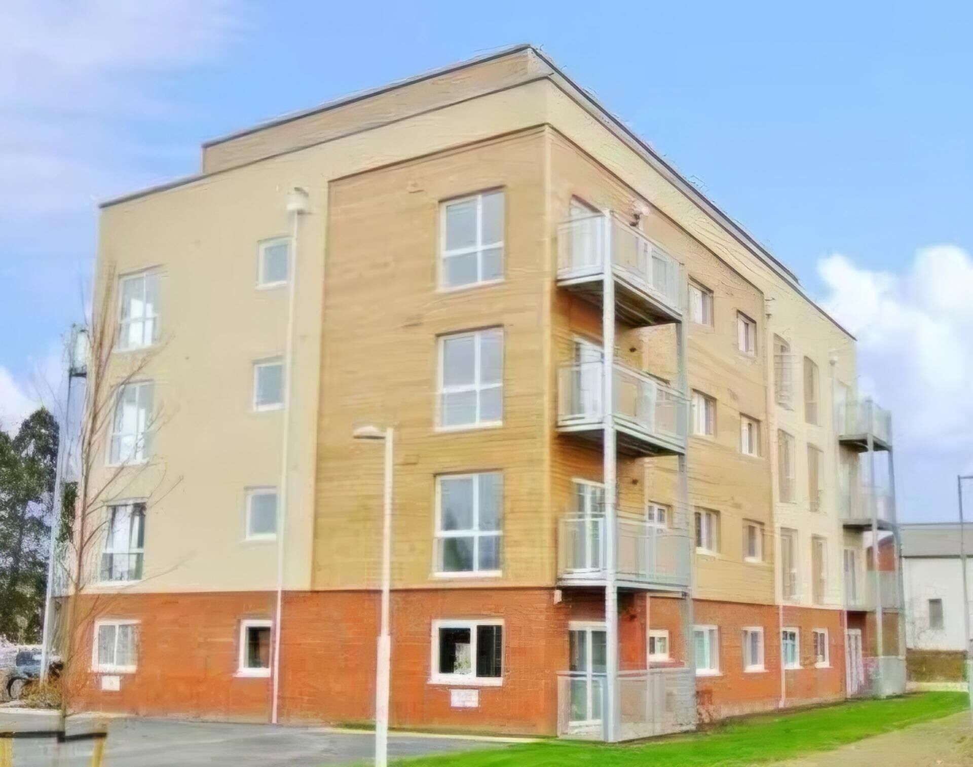 Un edificio de varios pisos con techo plano, ventanas rectangulares y un balcón en el segundo nivel.