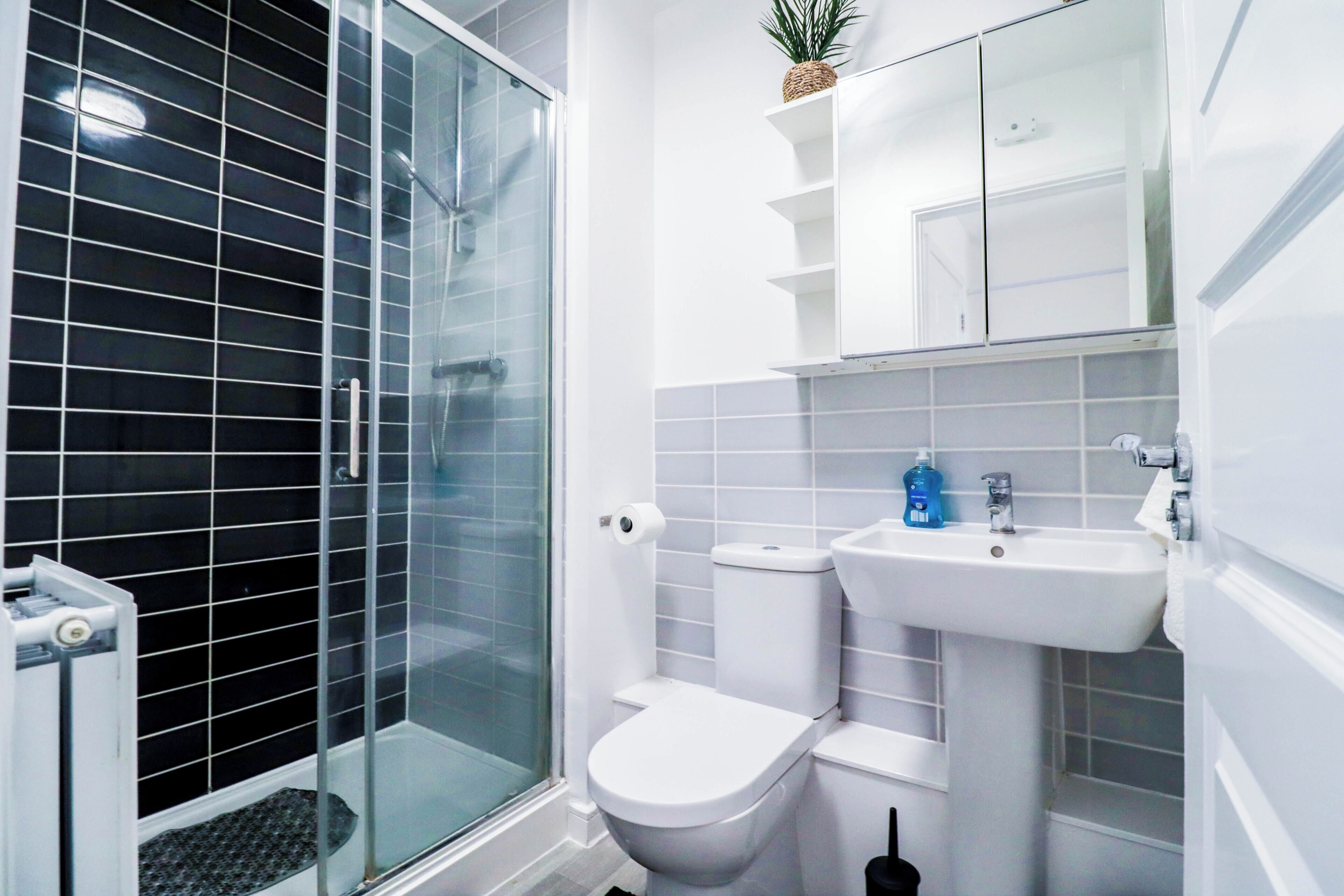 A modern bathroom with a glass shower enclosure, a toilet, a sink, and a small shelf with a plant.