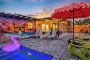 A pool area with lounge chairs, a flamingo float, and a mural of a butterfly and palm trees. - Saltwater Siesta Sarasota Private Home with Resort Style Backyard and Heated Pool, mini golf, fire pit, game room, near IMG, not far from beaches. 4BR/3BA, sleeps 10. (Sarasota)