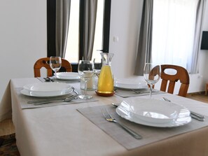 A dining table set with plates, cutlery, glasses, and a pitcher of yellow liquid, likely lemonade, in a room with wooden chairs and a window with curtains. - Charming Holiday Home With Terrace and Garden - One Bedroom Holiday Home (Moscenicka Draga)