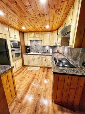 A kitchen with wooden cabinets, a stainless steel refrigerator, a microwave, an oven, a sink, and a granite countertop.