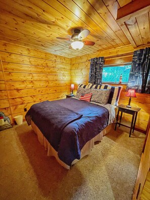 Une chambre à coucher dans un chalet en bois, avec un lit, une table de chevet, une lampe et une fenêtre avec des rideaux.