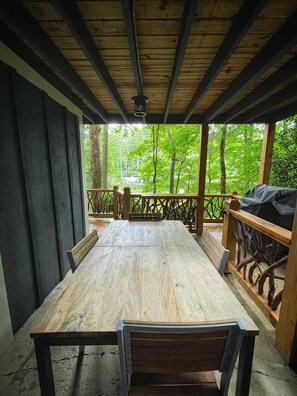 Un espace extérieur abrité, aménagé pour prendre les repas, avec une table et des bancs en bois, entouré d’une rambarde offrant une vue sur une zone boisée.