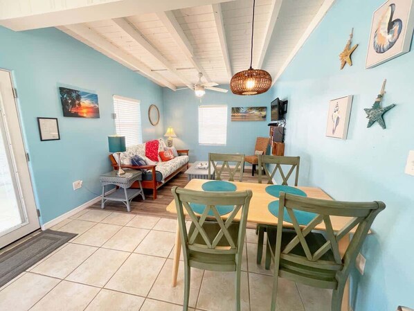 A dining area with a table and chairs, a ceiling fan, and wall art including starfish and a sunset painting.