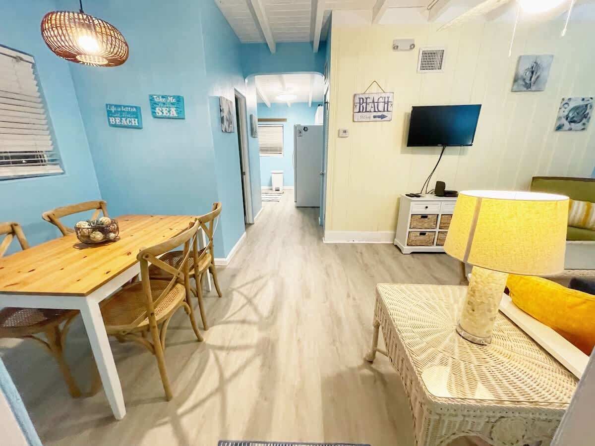A room with a wooden dining table, wicker chairs, a wicker side table, a television, and a sign that reads "BEACH".