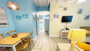 Una habitación con una mesa de comedor de madera, sillas de mimbre, una mesita auxiliar de mimbre, un televisor y un cartel que dice "BEACH".