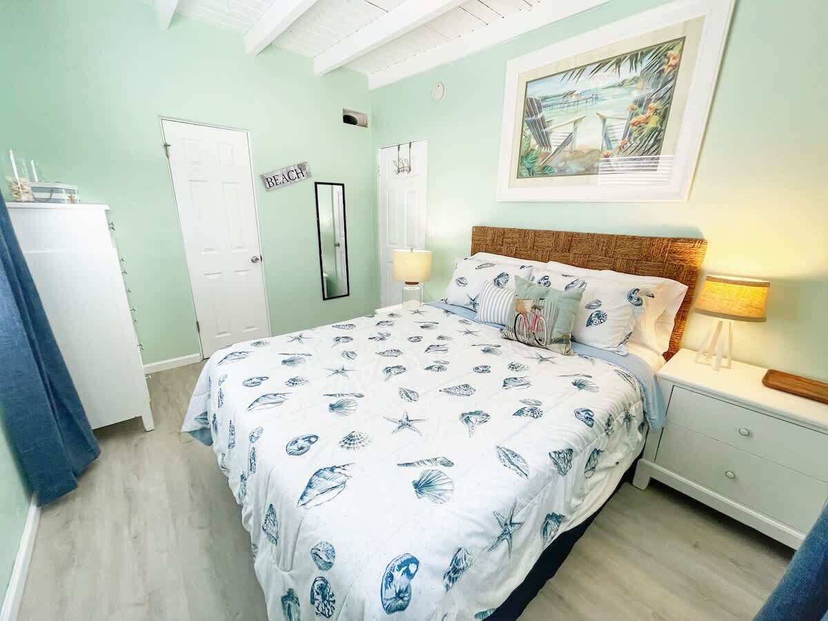Un dormitorio con cama, mesitas de noche, cómoda y una puerta.