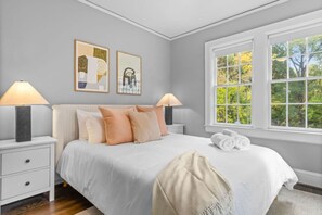 A bedroom with a bed, two bedside tables, a window with a view, and two wall-mounted artworks. - Modern Villa w Pool, Hot Tub & Games! (Greensboro)