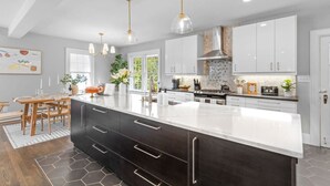 Une cuisine moderne dotée d’un grand îlot central, de meubles de couleur sombre et d’un éclairage suspendu.