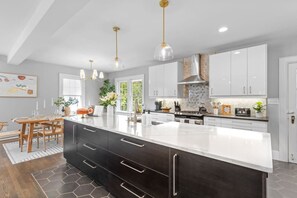 A modern kitchen with a large island, dark cabinetry, and pendant lighting.